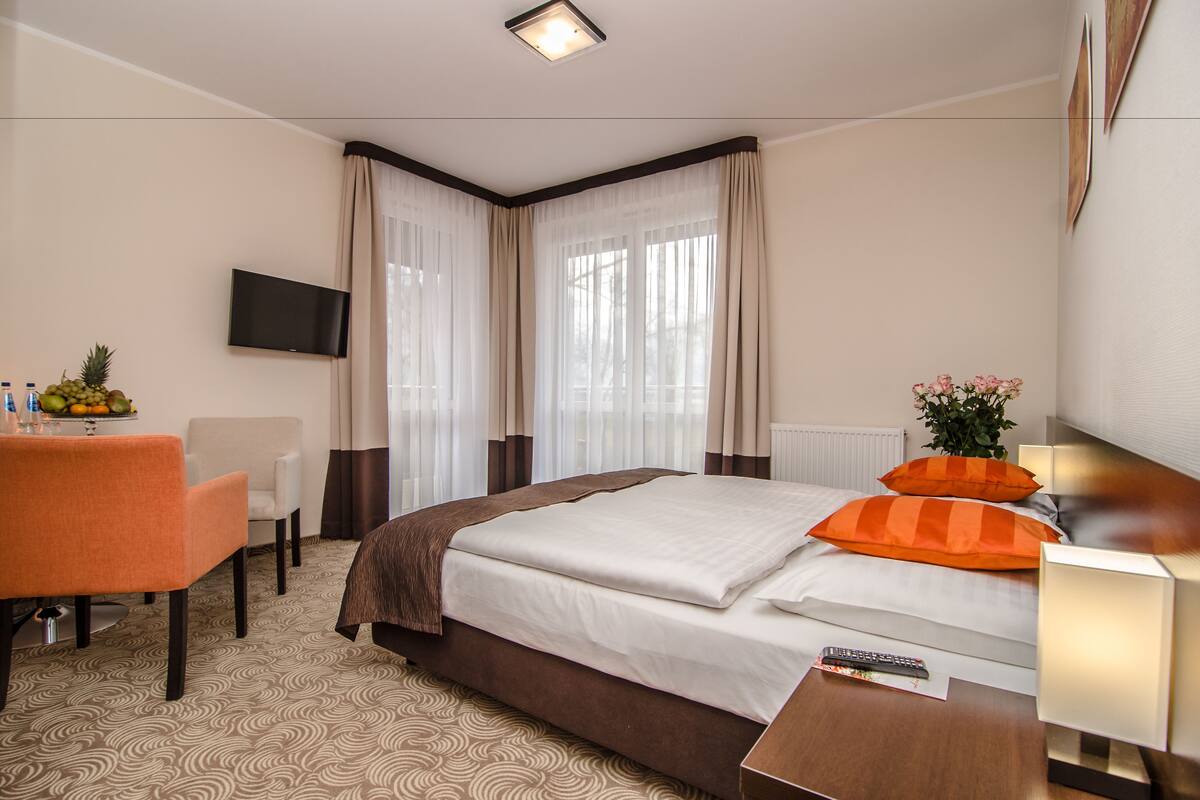 A hotel room with a bed, a desk, a chair, a TV, and a window with curtains.