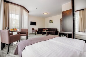 A hotel room with a large bed, a sofa, a desk with a chair, a TV, and a wardrobe. - Hotel Emocja SPA (Mielno)