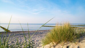 A beach with sand, grass, and a calm sea. - Hotel Emocja SPA (Mielno)