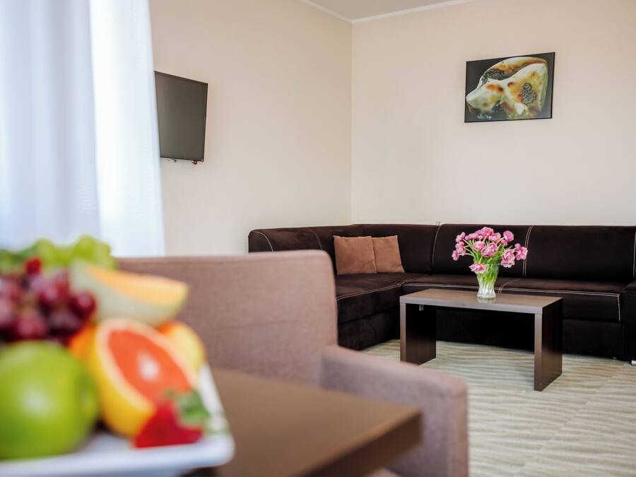 A modern living room with a brown leather sofa, a coffee table with a vase of pink flowers, and a fruit bowl on a side table.