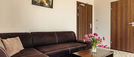 Una sala de estar moderna con un sofá seccional marrón, una mesa de centro de madera con un florero de flores rosas y dos puertas de madera.