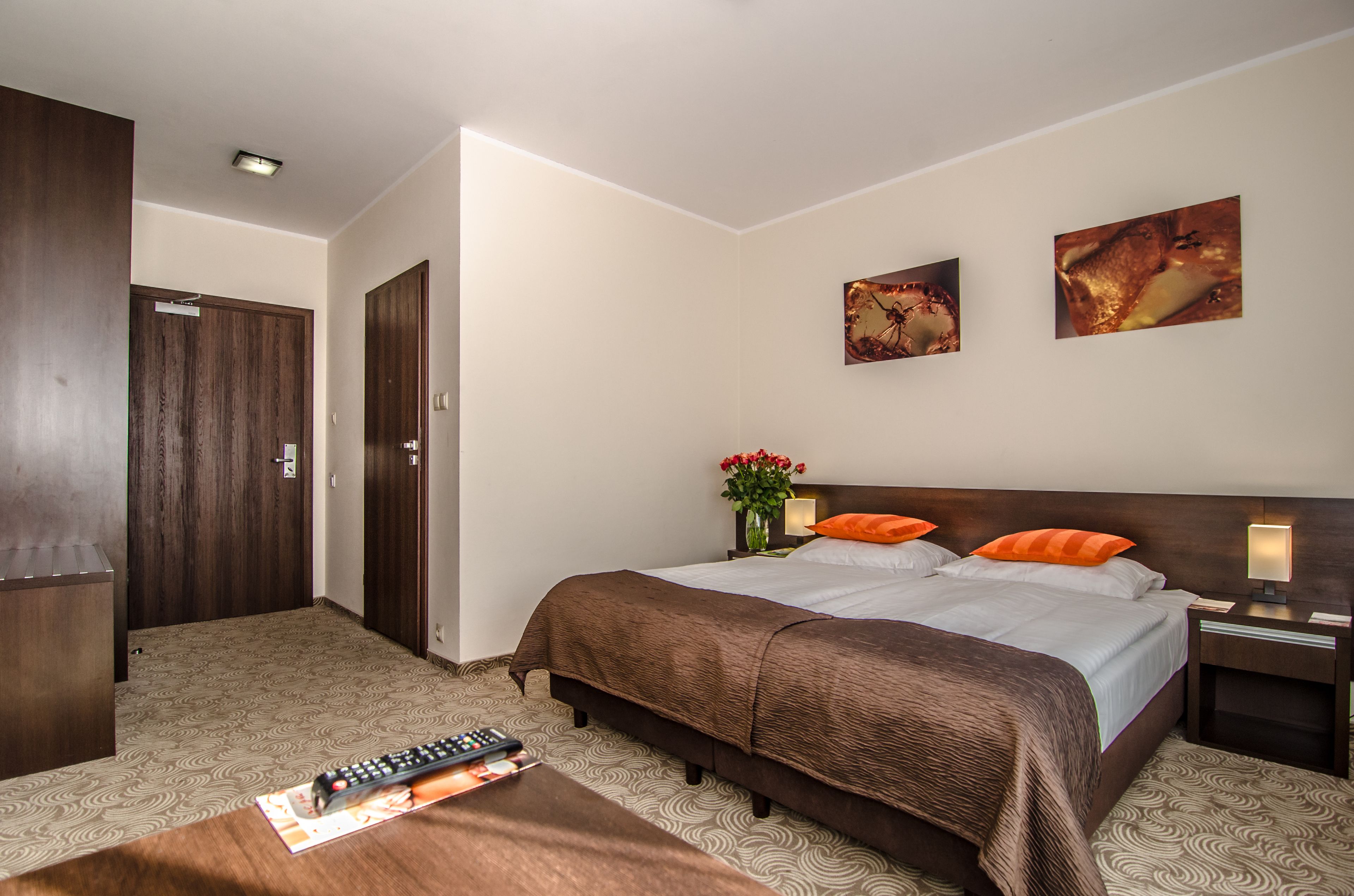 A hotel room with a large bed, two nightstands, a desk, a chair, a wardrobe, and two wall-mounted paintings.