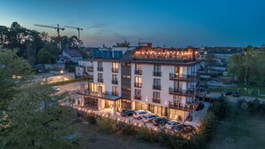 A multi-story hotel with balconies, a parking area, and a construction crane in the background. - Hotel Emocja SPA (Mielno)
