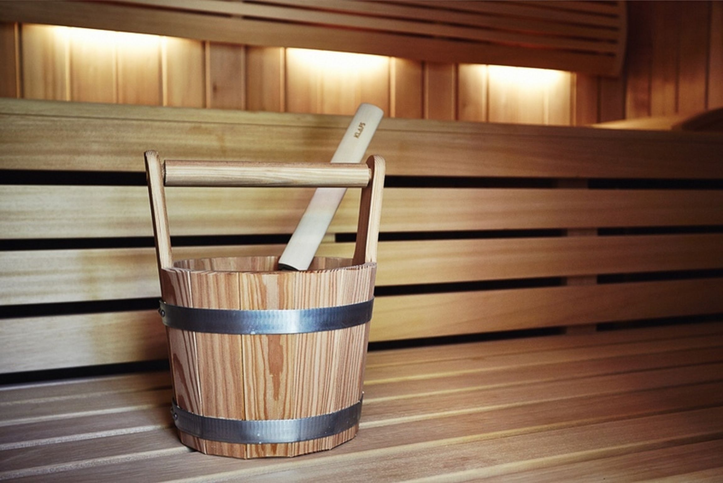 Un banco de madera con un balde de metal que contiene un palo de madera.
