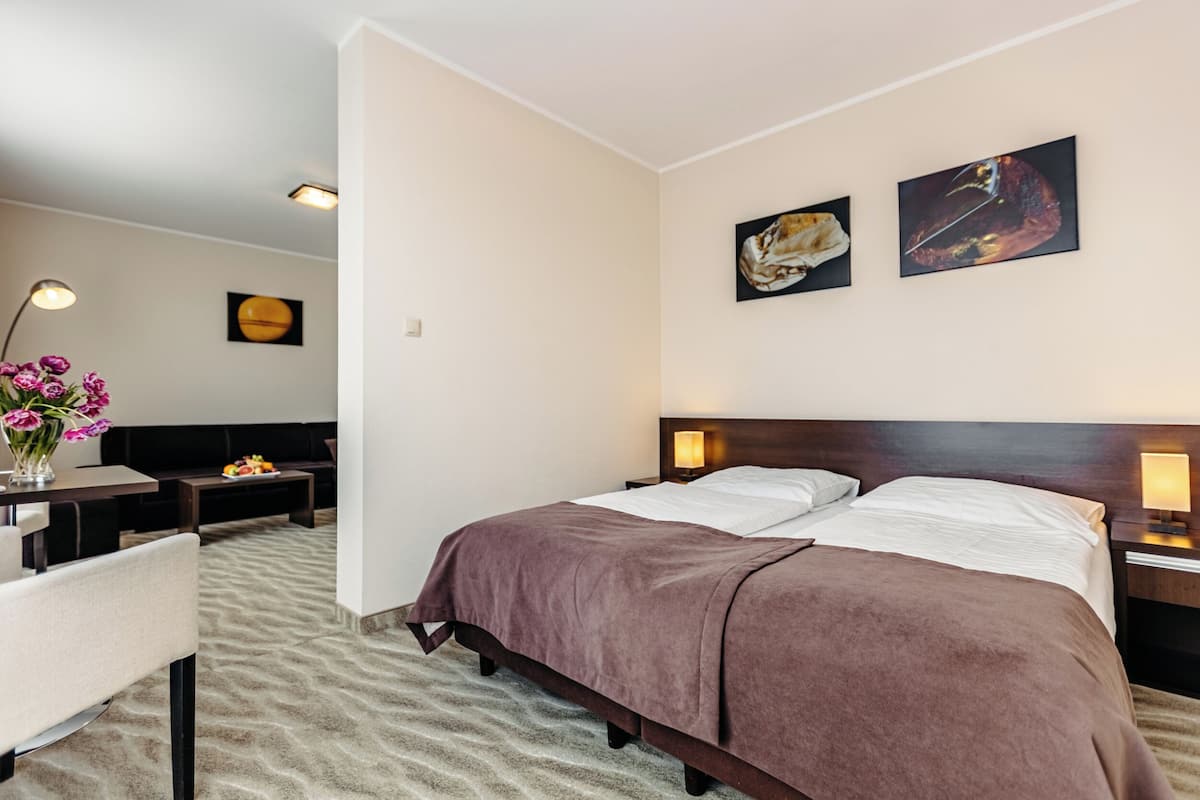 A hotel room with a bed, a desk, a chair, and two wall-mounted paintings.