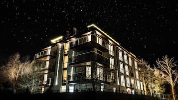 Un edificio de varios pisos con balcones y ventanas amplias, rodeado de árboles.