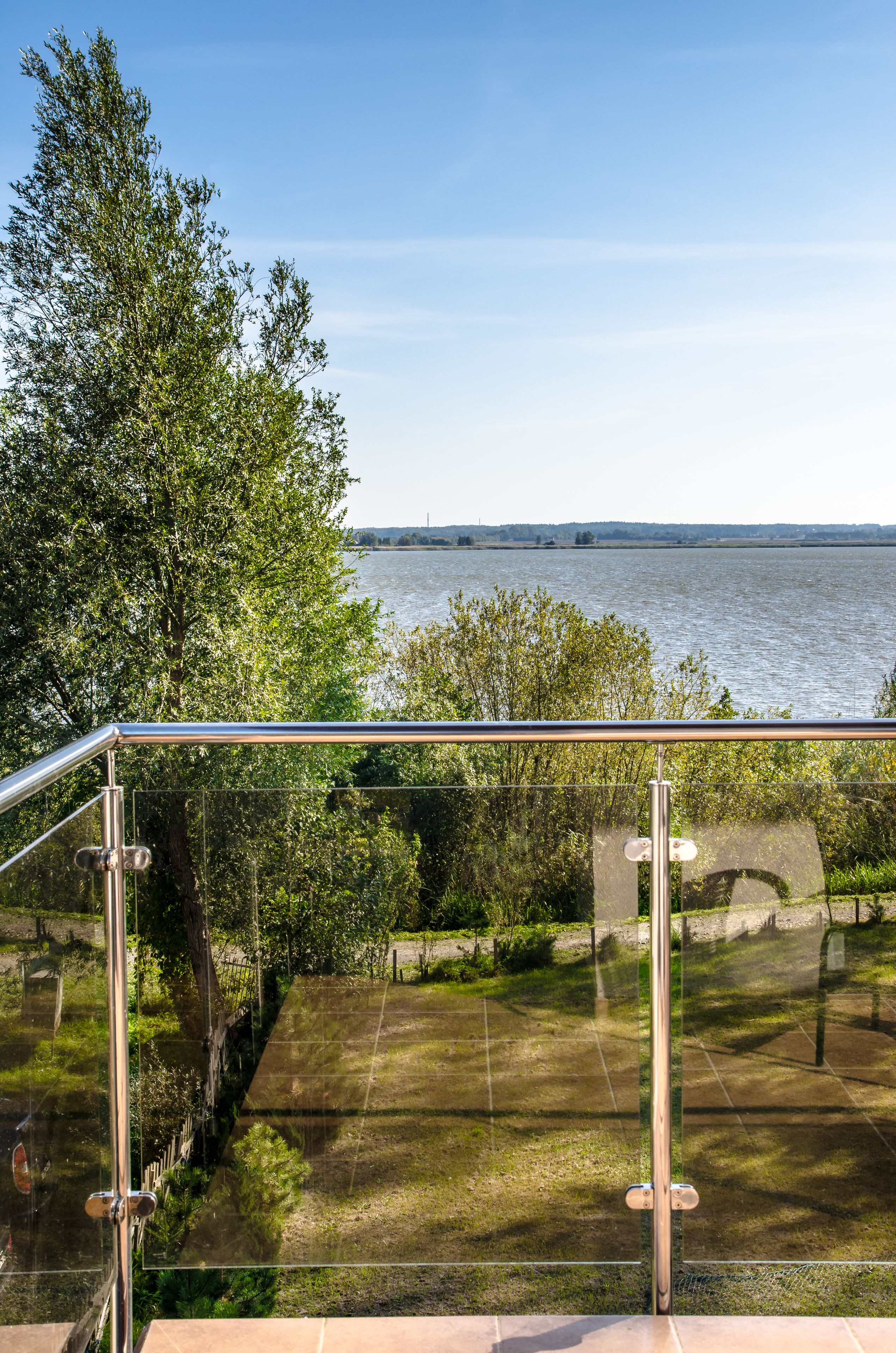 Een balkon met glazen hekwerk en uitzicht op een wateroppervlak, omringd door groen.