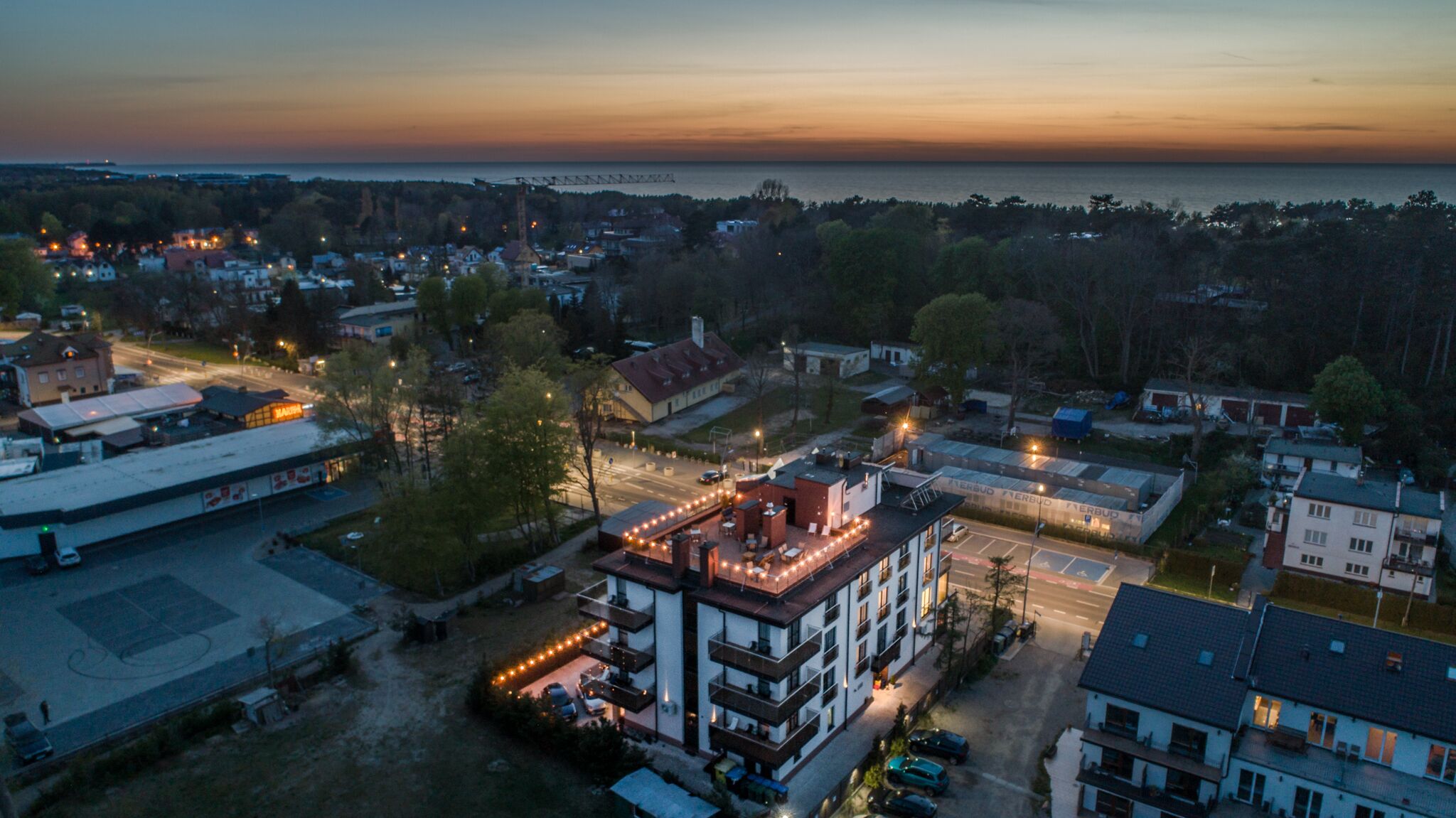 An aerial view of a residential area with a prominent building featuring balconies and a rooftop terrace.