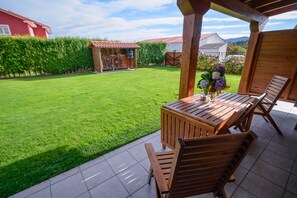 Une terrasse en bois avec une table et des chaises, un abri de jardin en bois et une pelouse bien entretenue.