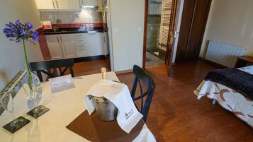 Habitación de hotel con una mesa de comedor para dos, una cocina al fondo y una cama con colcha estampada.