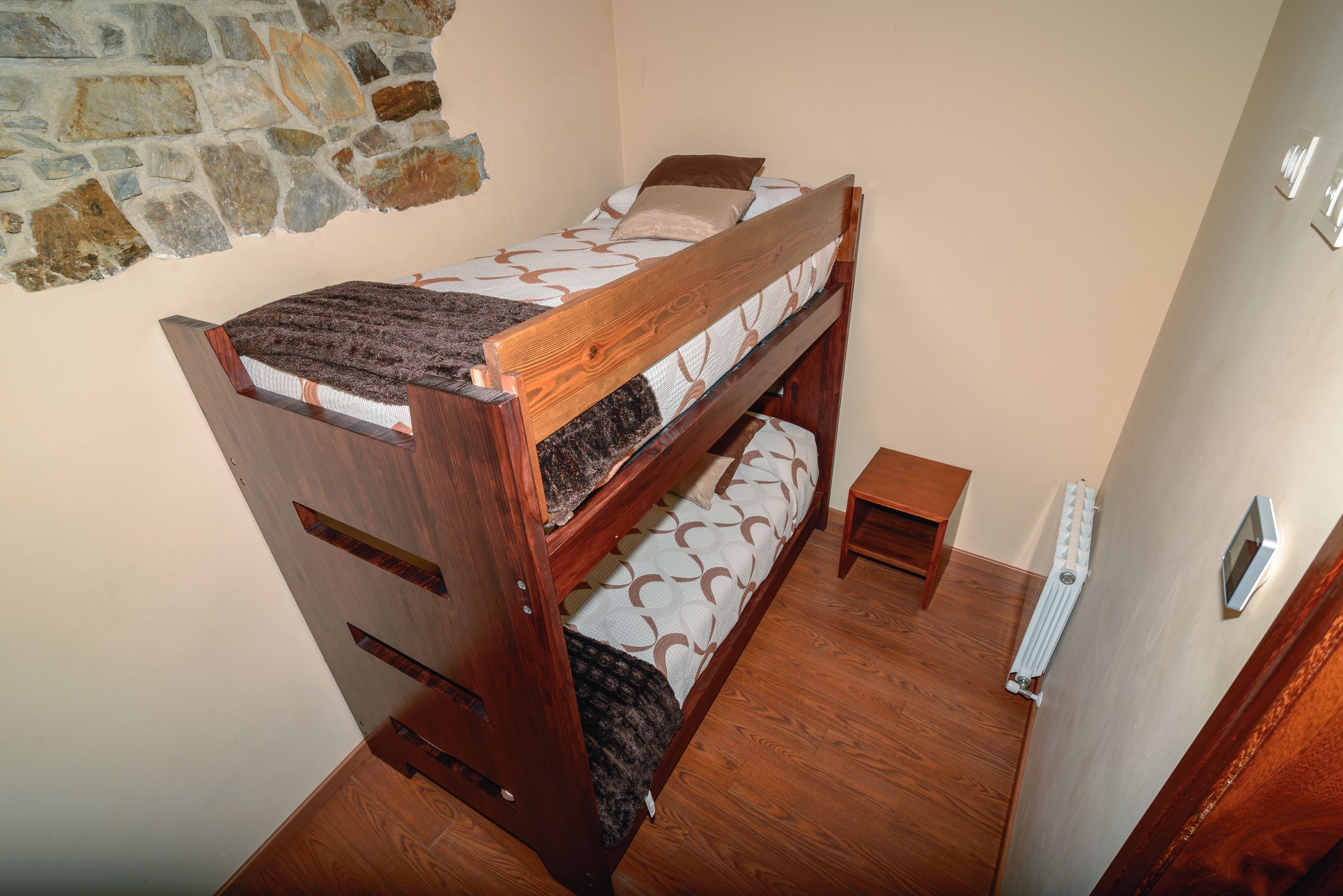 A bunk bed with a wooden frame, a small bedside table, and a radiator on the wall.