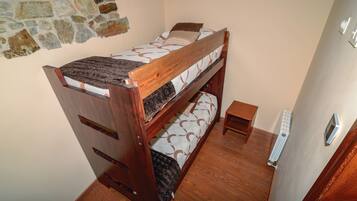 A bunk bed with a wooden frame, a small bedside table, and a radiator on the wall.