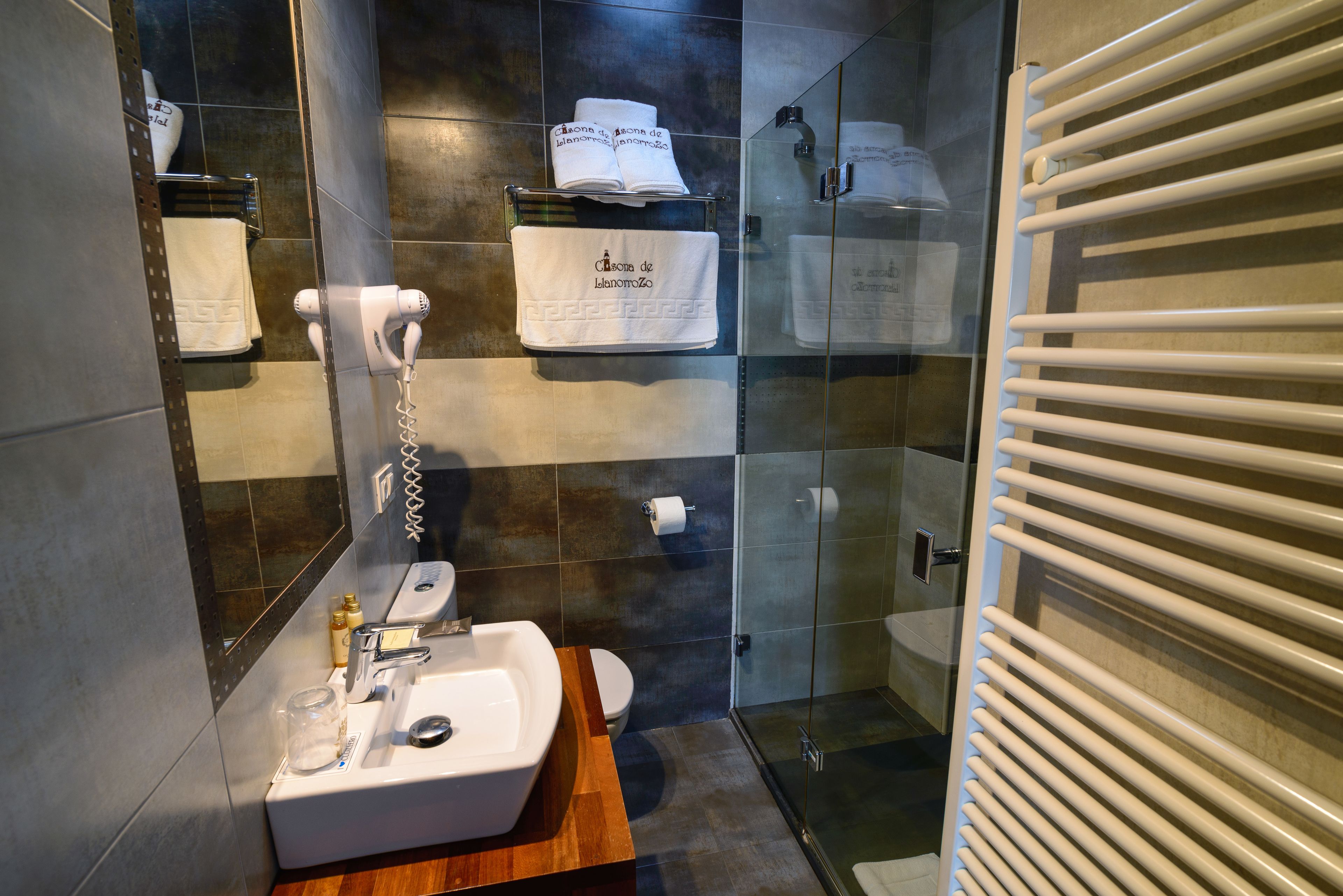 Un baño moderno con cabina de ducha de vidrio, un lavabo blanco y un toallero con toallas dobladas.