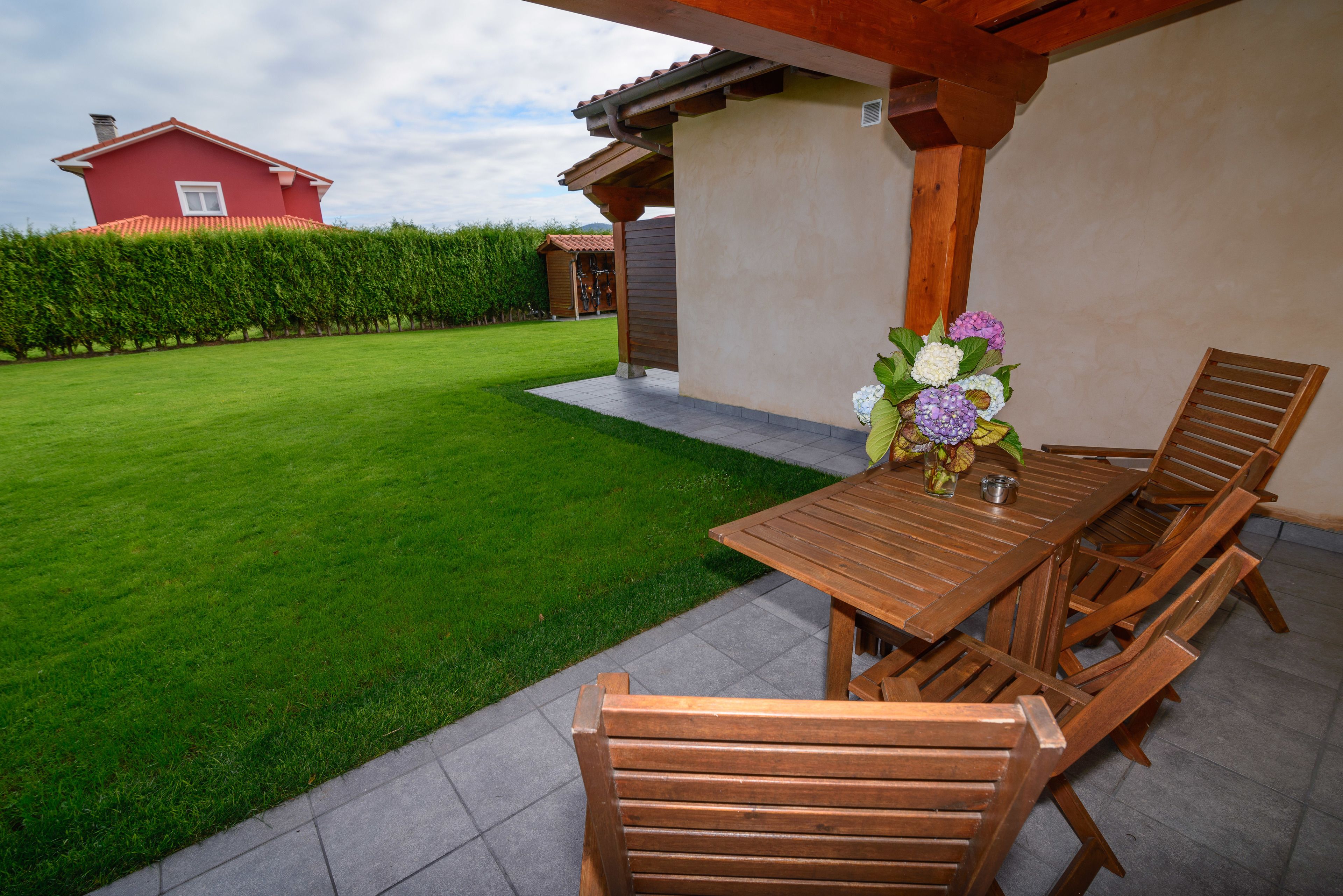 A wooden table with chairs and a vase of flowers in a garden area.