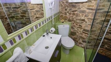 Et badeværelse med stenvæg, hvid vask, toilet og brusekabine i glas.
