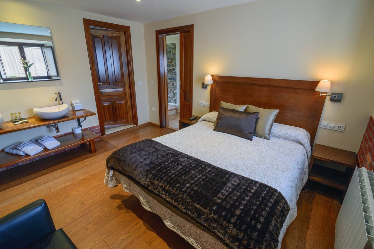 Une chambre à coucher avec un grand lit, une tête de lit en bois, des lampes de chevet, un lavabo intégré et un miroir.