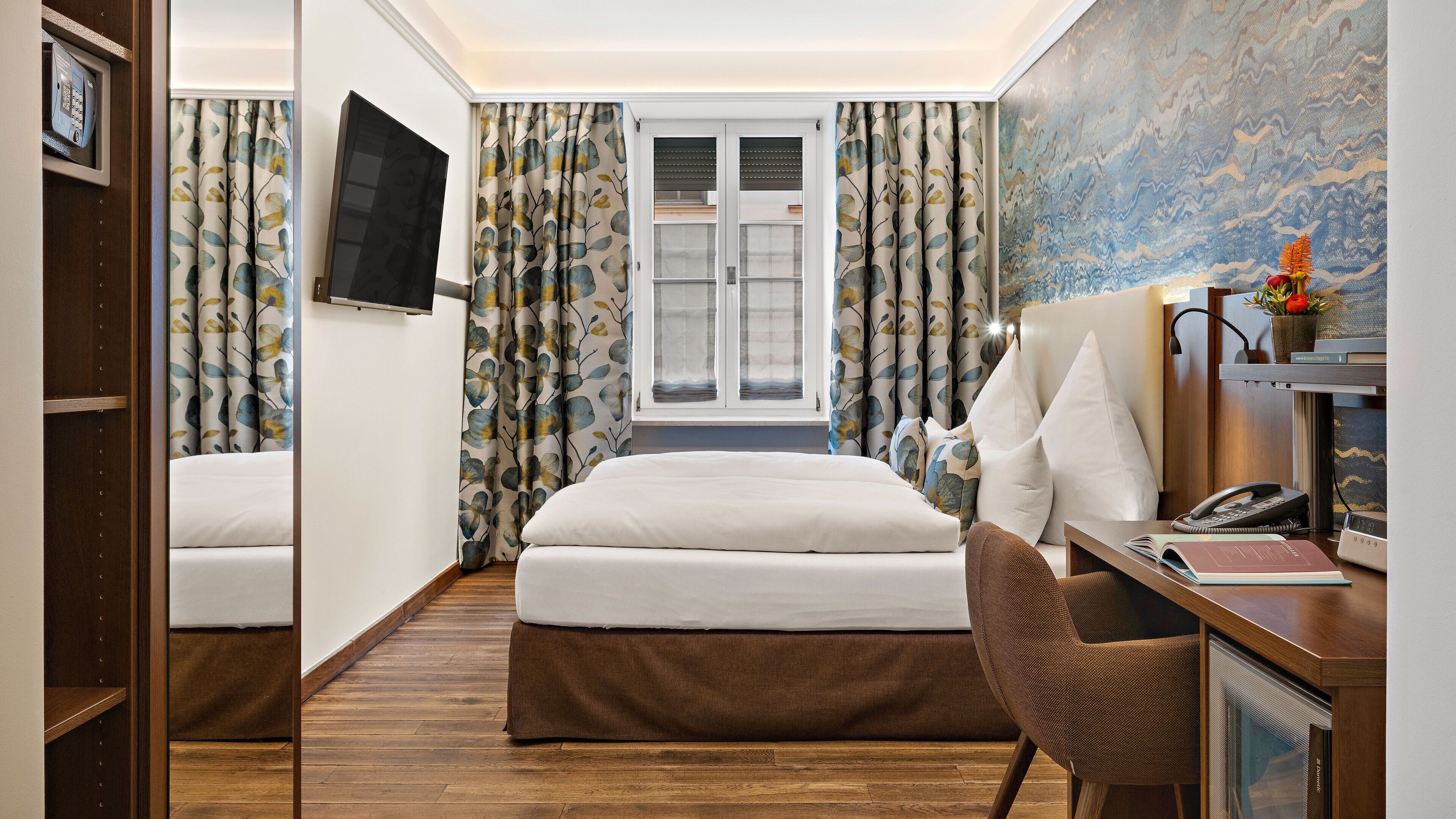 Een hotelkamer met een bed, een bureau, een stoel, een televisie en een raam met gordijnen.