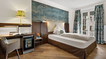 A hotel room with a bed, desk, chair, and a painting on the wall.