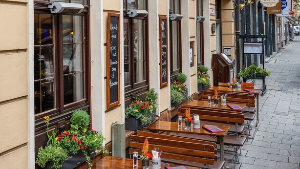 A row of wooden tables and benches outside a building with the sign "Deutsche G\u00f6be". - Hotel Deutsche Eiche (Munich)
