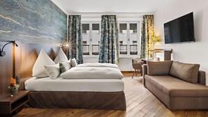 A modern hotel room with a large bed, a sofa, a desk, and a TV. - Hotel Deutsche Eiche (Munich)