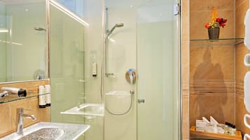 Un baño moderno con ducha envuelta en vidrio, lavamanos de mármol y repisa de vidrio con artículos de aseo.
