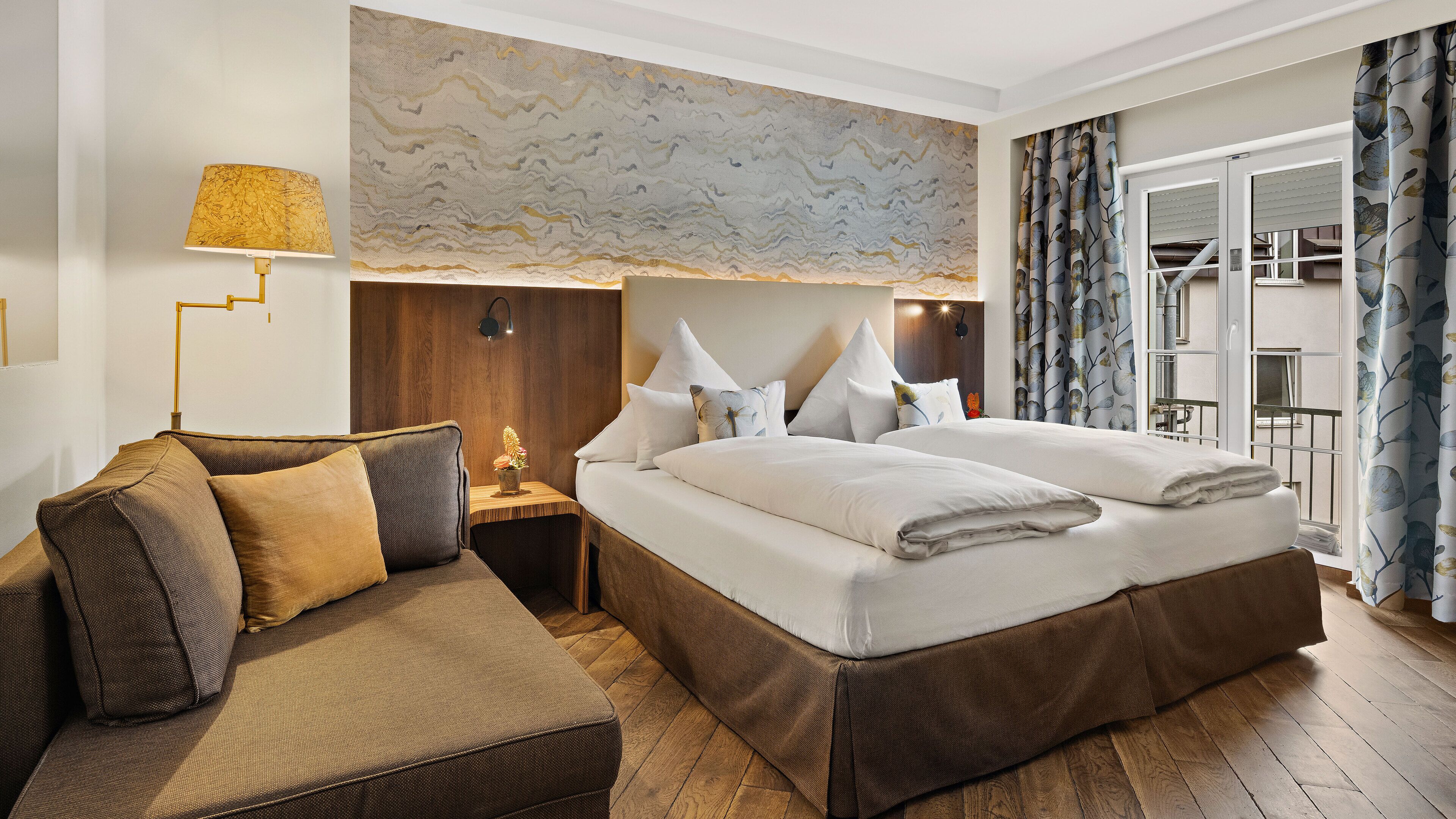A modern hotel room with a large bed, a sofa, a nightstand, and a marble wall.