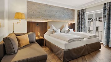 A modern hotel room with a large bed, a sofa, a nightstand, and a marble wall.