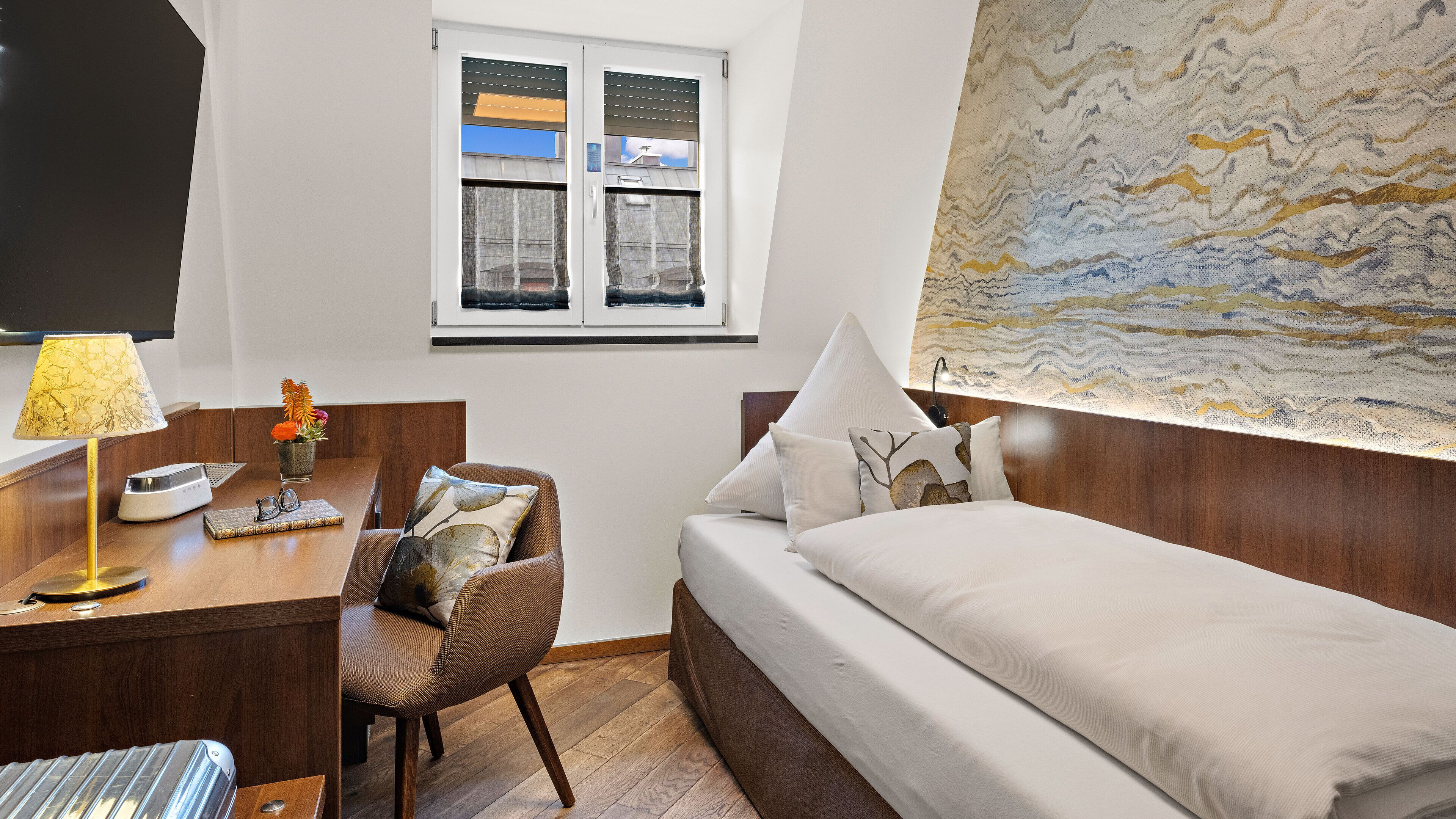 Un dormitorio con cama, escritorio, silla, lámpara y ventana con persianas.