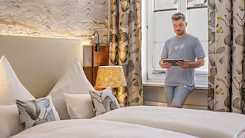 A hotel room with a bed, pillows, a bedside lamp, and a window with curtains.