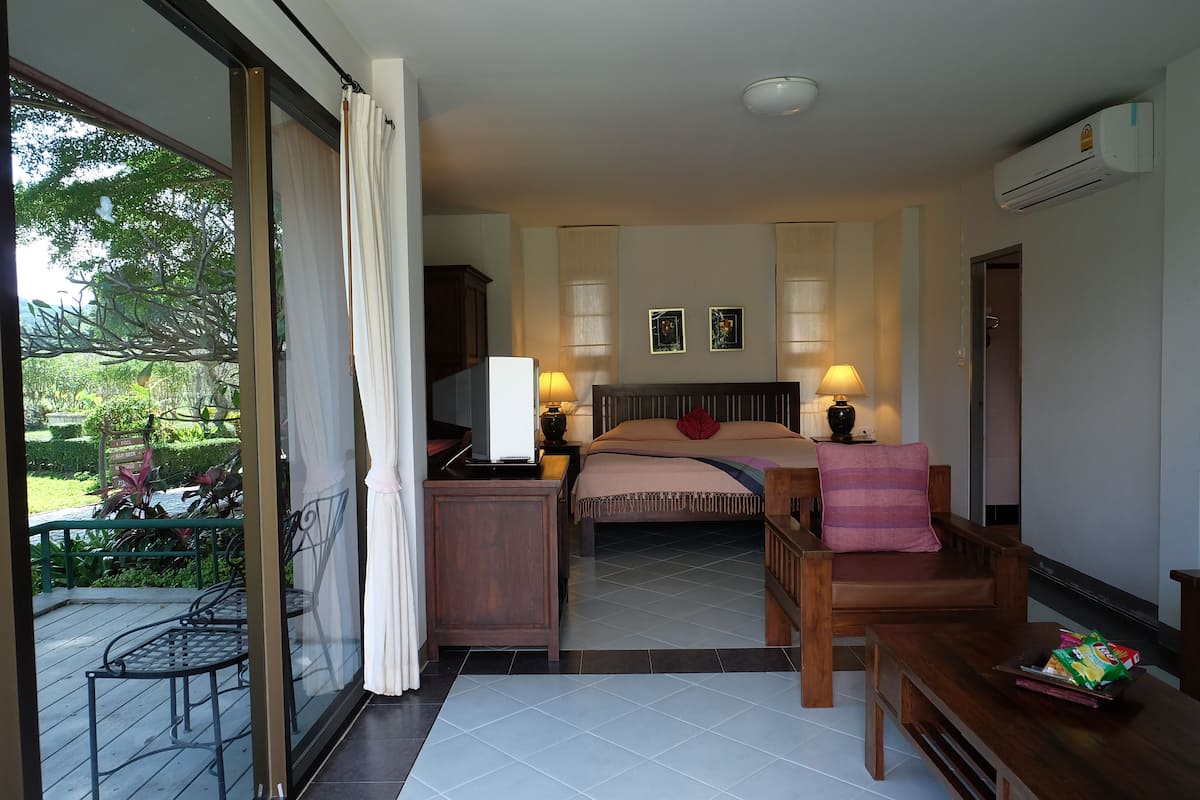 A bedroom with a bed, a wooden chair, a nightstand, and a table with a bag of snacks.