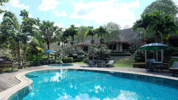 Una piscina con cubierta de madera, rodeada de palmeras y sillones de descanso.