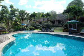 A swimming pool with a wooden deck, surrounded by palm trees and lounge chairs. - Lilawalai Resort (Pak Chong)