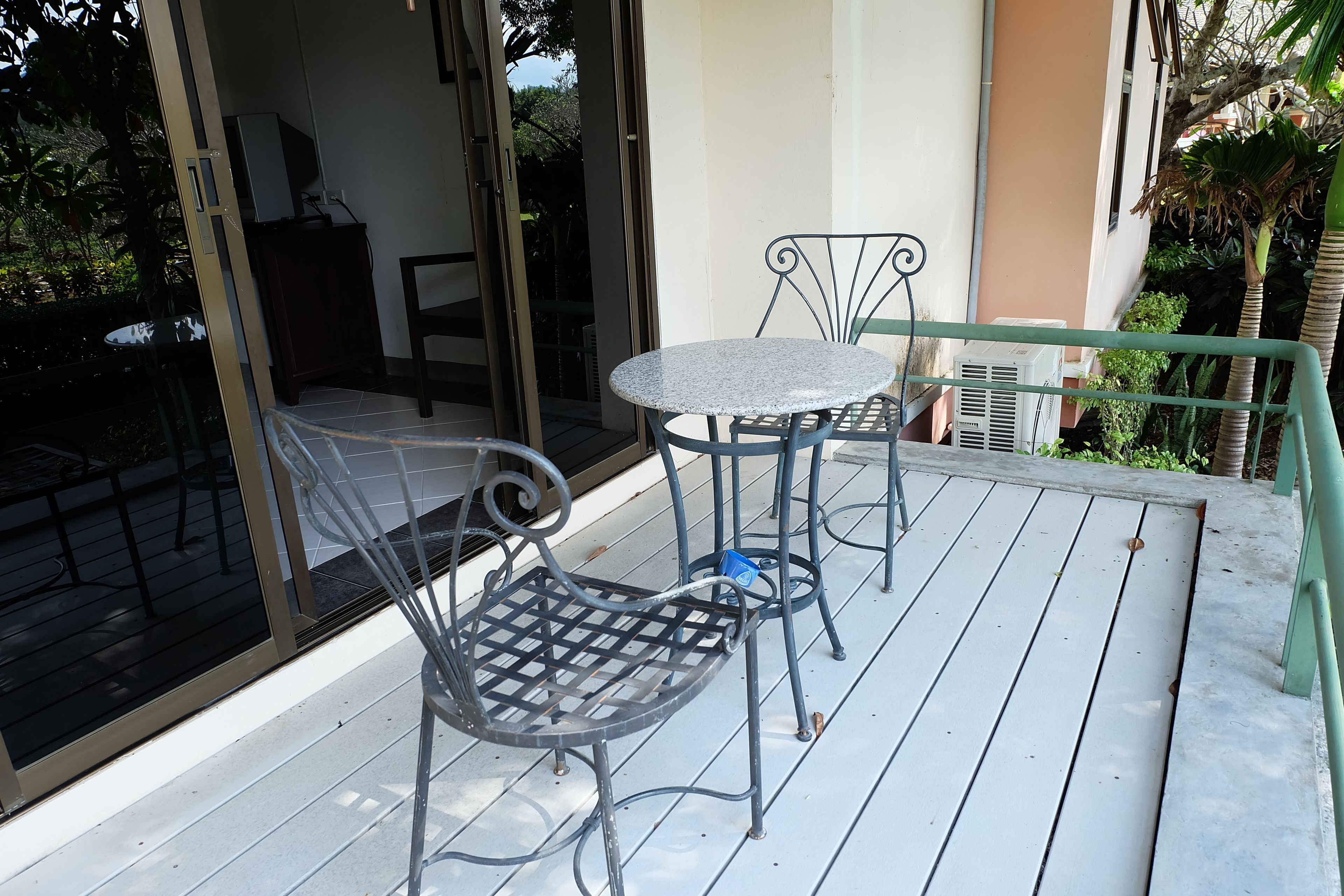 Een balkon met een tafel en twee stoelen, een schuifdeur en uitzicht op groen.