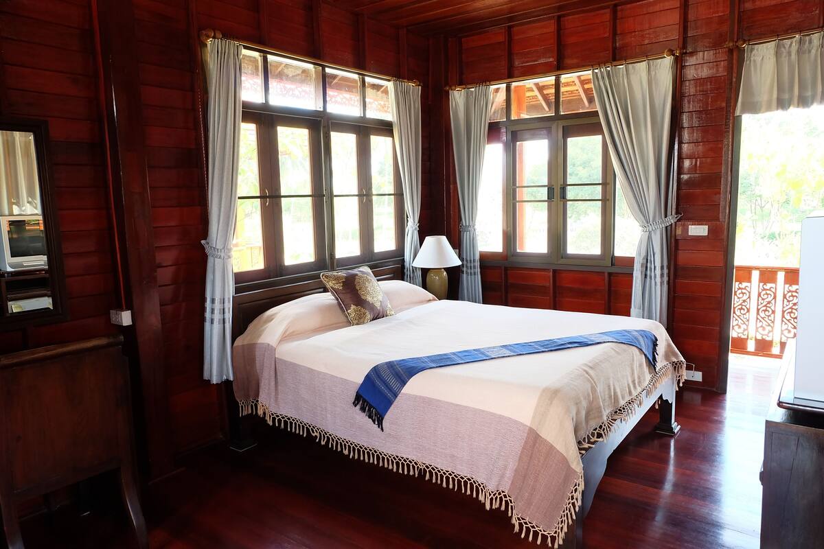 A wooden room with a bed, a lamp, and curtains.