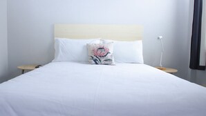 Una cama bien tendida con sábanas blancas, un cojín decorativo y dos mesitas de noche con lámparas.