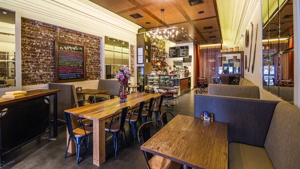 Un interior de restaurante acogedor con mesas y sillas de madera, una zona de bar y un menú en la pizarra.
