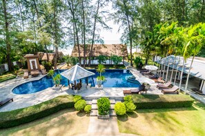A large outdoor swimming pool surrounded by lounge chairs, a gazebo, and a thatched-roof building. - Ocean Breeze Residence (Takua Pa)