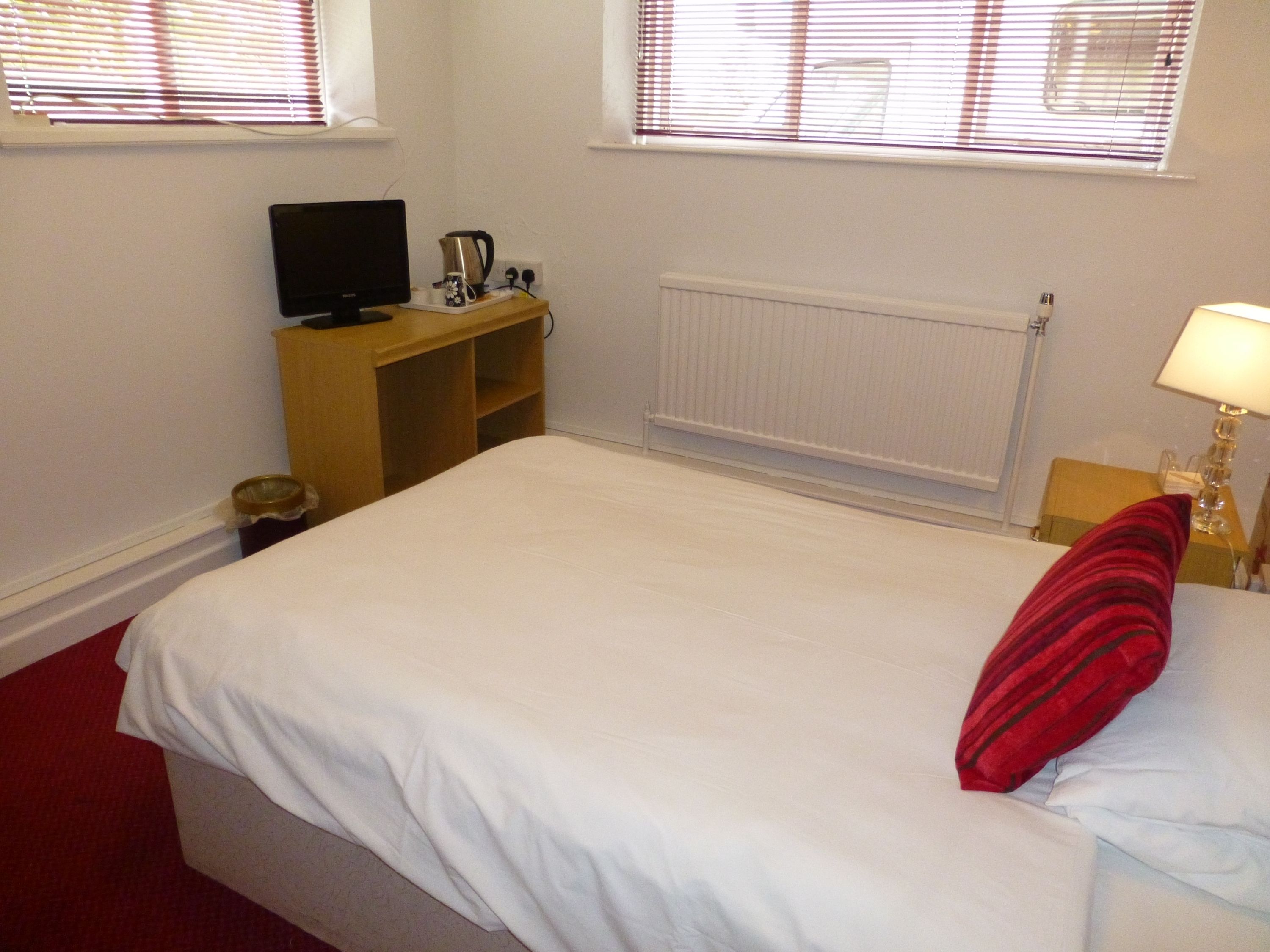 A bedroom with a bed, a TV, a coffee maker, and a radiator.