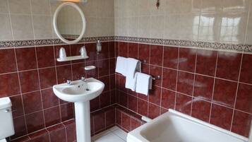 A bathroom with a white sink, a toilet, and a bathtub. There is a mirror above the sink and a towel rack with a towel hanging on it. The walls are tiled with a red pattern.