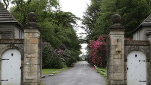 A stone gatehouse with arched doors, leading to a pathway flanked by lush greenery and flowering bushes. - Maes Manor Hotel (Blackwood)