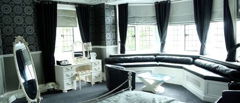A bedroom with a bed, a vanity with a mirror, a dresser, a black leather bench, and a chandelier.