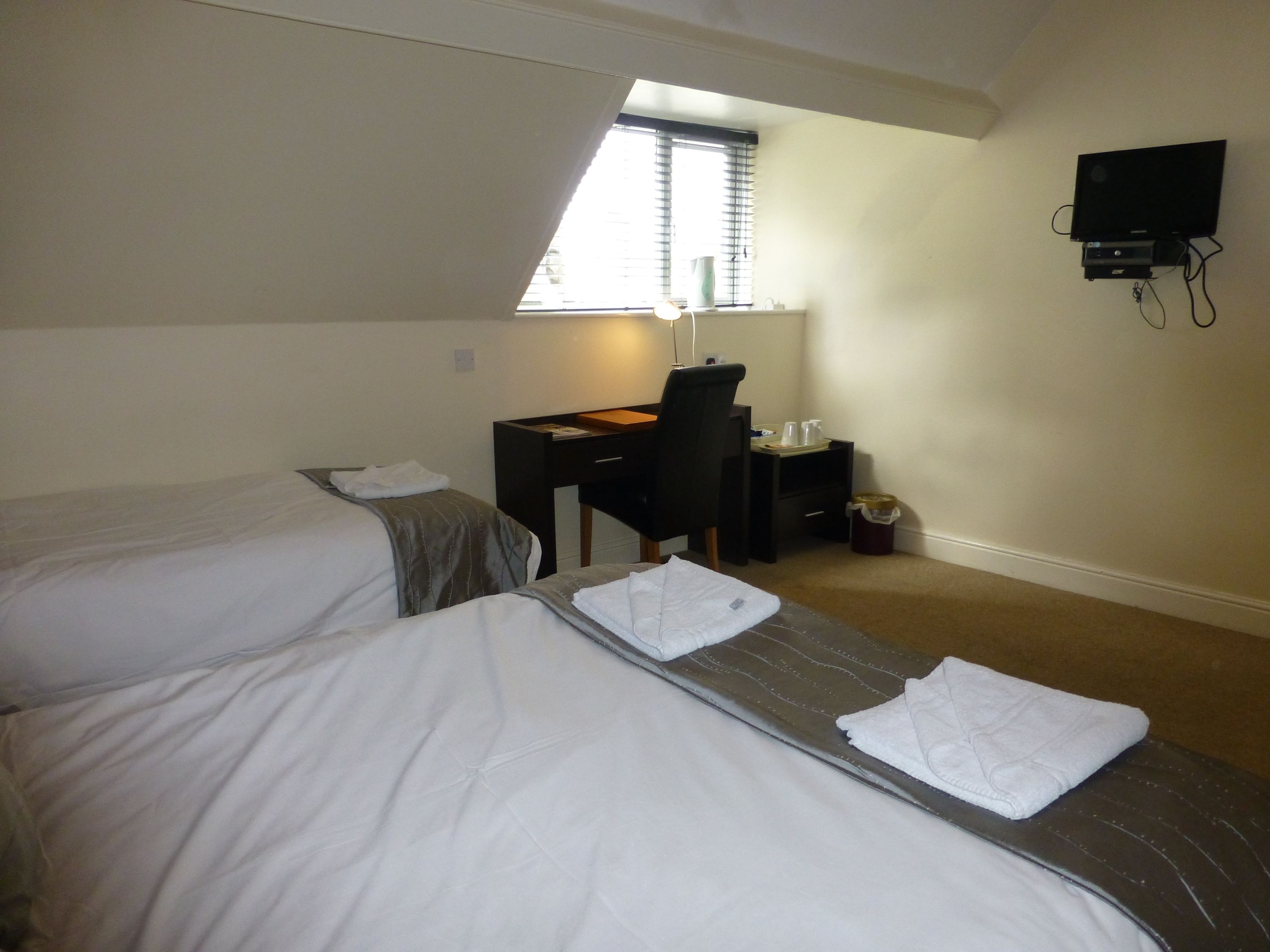 A hotel room with two beds, a desk, a chair, a TV, and a window with blinds.