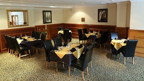 A dining area with multiple tables, black chairs, and patterned floor tiles. - Maes Manor Hotel (Blackwood)