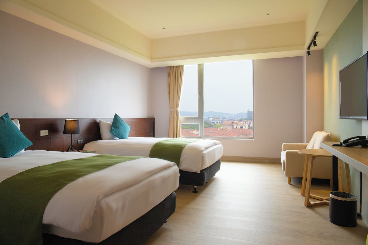 Een hotelkamer met twee bedden, een bureau, een stoel, een televisie en een groot raam met uitzicht.