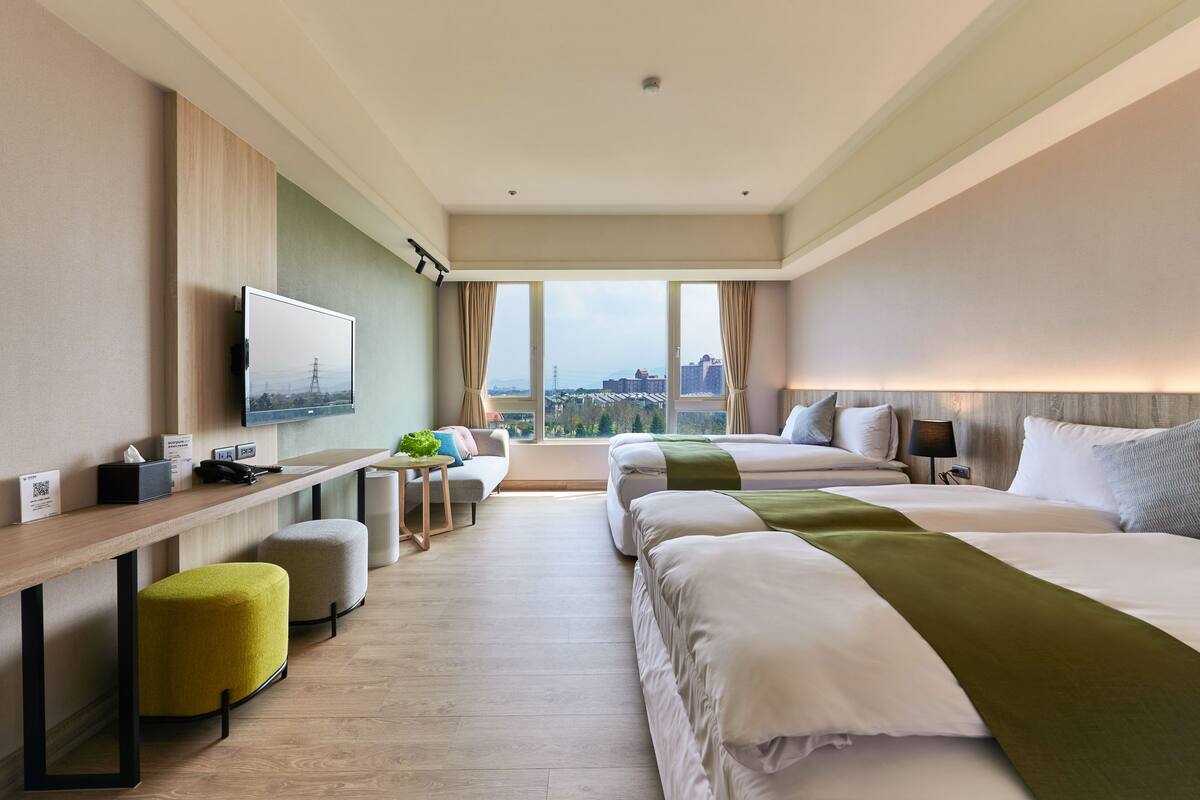 Een hotelkamer met twee bedden, een bureau, een televisie en uitzicht op de stad.