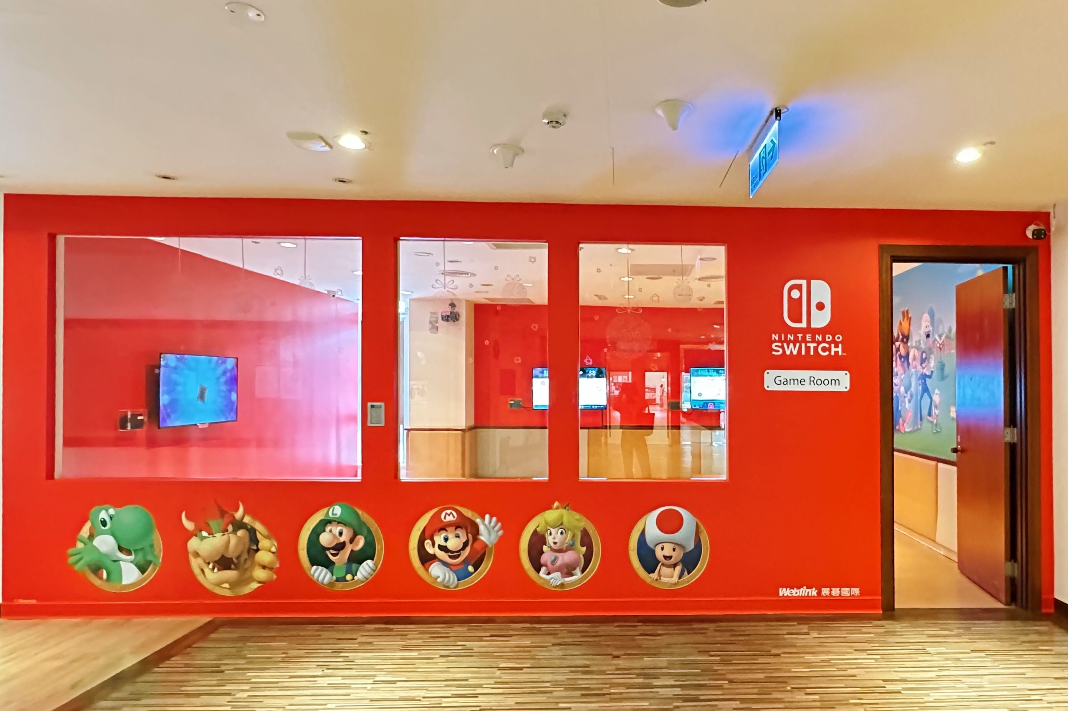 Pared roja con logotipos de Nintendo Switch y letrero de sala de juegos.