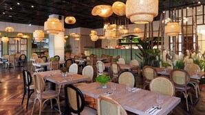 A restaurant with wooden tables and chairs, hanging wicker lamps, and a bar area in the background. - Aspire Resort (Taoyuan City)