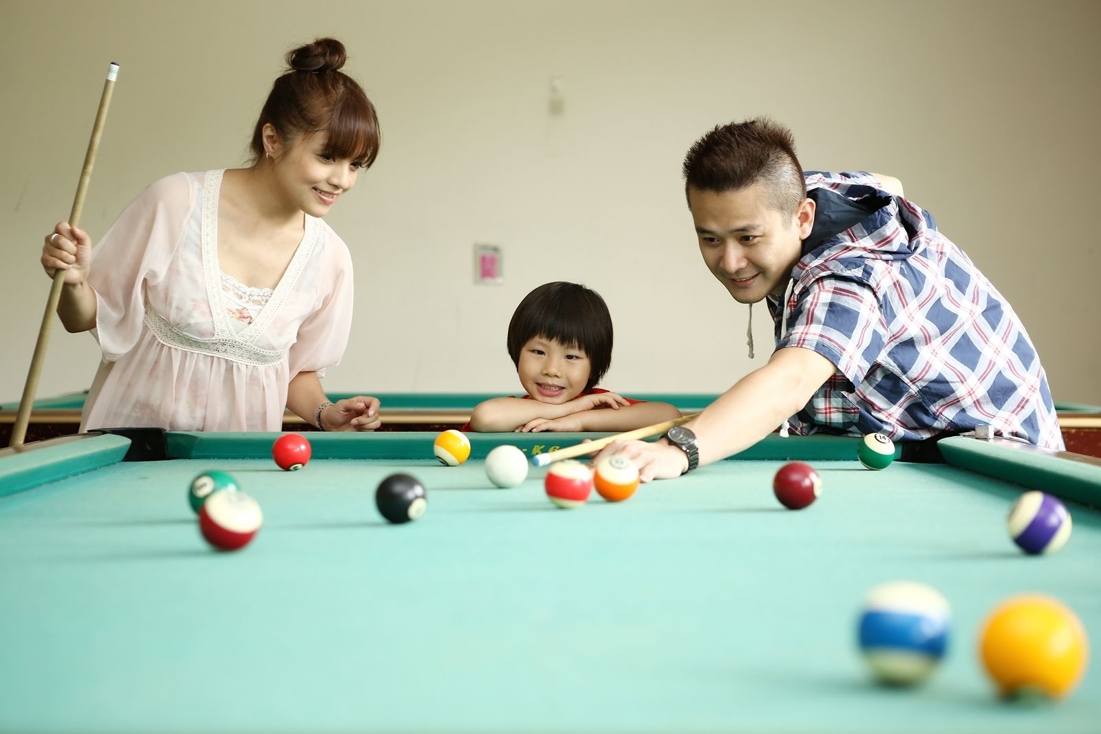A pool table with balls, a person holding a cue stick, and another person leaning over the table.