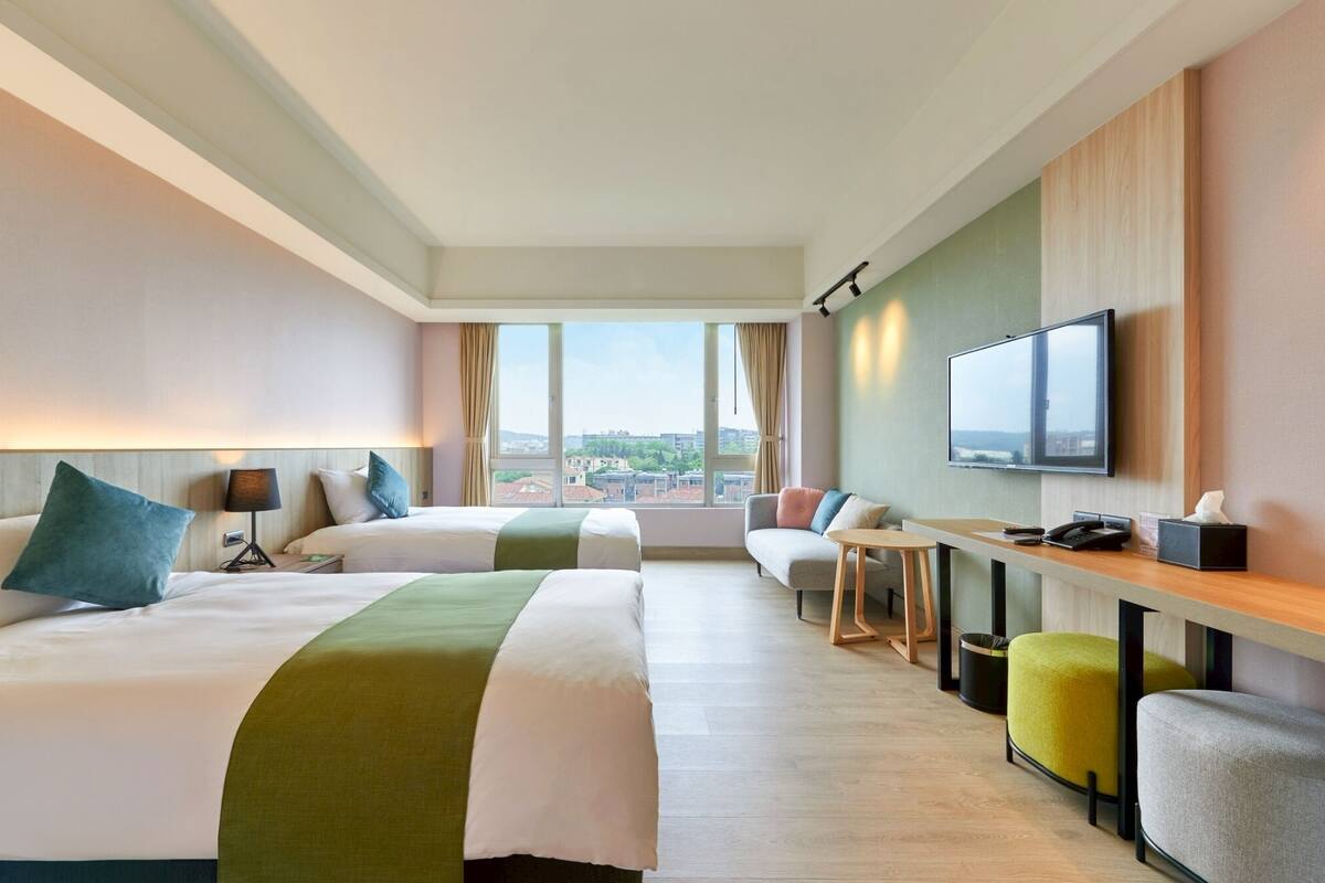 Een hotelkamer met twee bedden, een bureau, een televisie en uitzicht op de stad.