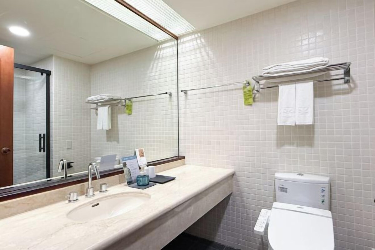 A modern bathroom with a large mirror, two sinks, a toilet, and a towel rack.
